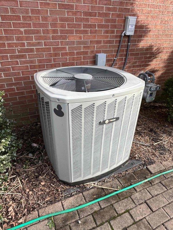 Performed on-site evaluation of existing 15-year-old Trane air conditioning condenser unit and matching furnace system for complete HVAC replacement estimate. Inspected outdoor condenser unit located on brick paver pad against exterior wall, assessed electrical disconnect and utility connections, and documented current system configuration. Evaluated indoor air handler and furnace installation in basement utility area, reviewed existing ductwork connections, and photographed equipment specifications for accurate replacement system sizing and proposal development.