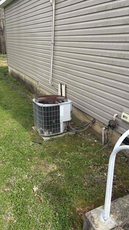 Conducted comprehensive HVAC replacement estimate for residential property with 29-year-old existing system. Evaluated outdoor condensing unit with protective cage guard positioned on concrete pad against building exterior, assessed refrigerant line routing and electrical connections, and documented propane tank location on property for system planning considerations. Homeowner requested full replacement options only with no repair alternatives.
