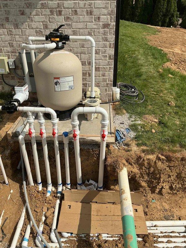 Completed electrical installation for new pool equipment system. Installed conduit and wiring from green electrical control box mounted on exterior brick wall to pool filtration equipment, including connections for sand filter tank with black valve assembly and manifold piping system with multiple ball valves. All electrical connections made to code specifications to support pool pump and filtration system operation.