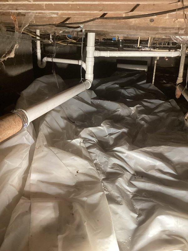 Conducted follow-up site visit to assess disconnected drain lines from toilet and bathtub that were actively draining into the crawlspace. Documented existing plumbing conditions including failed PVC drain connections and improper drainage routing beneath the structure. Photographed crawlspace plumbing system showing vapor barrier installation, exposed floor joists, and compromised drain assembly requiring immediate replacement to prevent structural damage and restore proper wastewater conveyance.