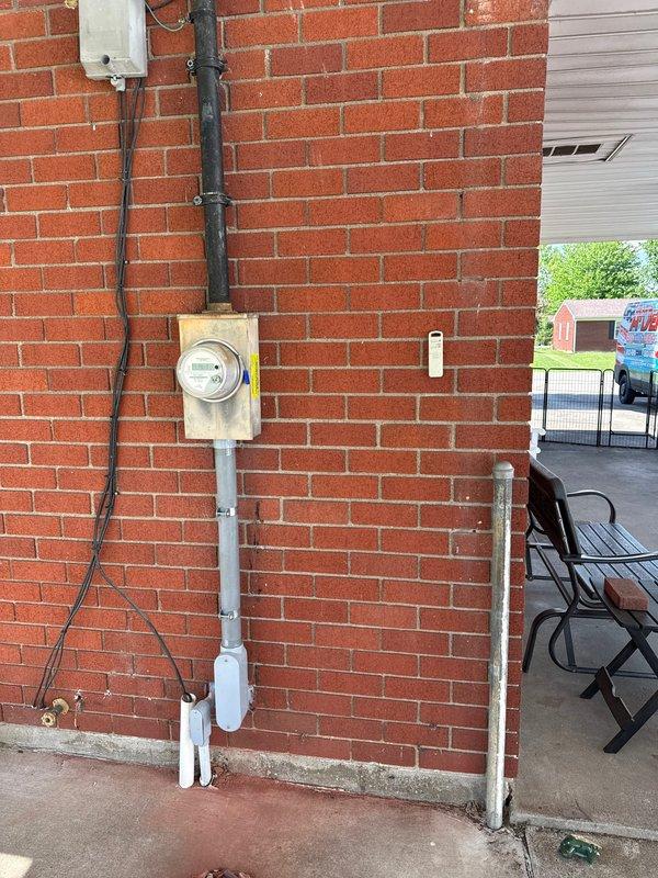 Completed electrical service upgrade including replacement of main electrical panel and utility meter. Installed new gray metal panel box in interior utility space with proper mounting and secure connections, ran necessary conduit and wiring from exterior meter location through building structure to new panel. Replaced exterior weathered meter assembly with updated equipment, ensuring proper weatherhead connections and conduit routing along brick exterior wall. Additionally replaced interior light fixture per customer request. All work completed to code with proper grounding and circuit protection, system tested and verified operational.