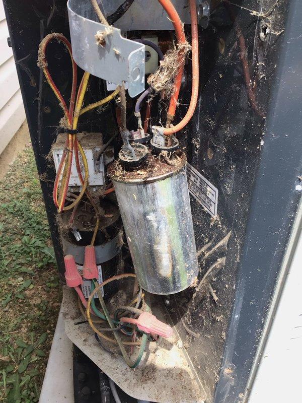 Responded to a no-cooling complaint on a 16-year-old residential air conditioning system. Upon arrival, performed visual inspection of outdoor condensing unit and removed access panel to assess internal components. Found capacitor exhibiting severe deterioration with corroded terminal connections, degraded wiring, and accumulated debris throughout the electrical compartment. Interior housing showed extensive dirt buildup, biological growth, and corrosion on multiple metal surfaces, indicating prolonged lack of maintenance and exposure to elements. Documented unit condition with photographs showing compromised electrical connections, particularly at capacitor terminals where orange wire displayed significant deterioration. System age and component condition suggest end-of-service-life status requiring comprehensive evaluation for repair versus replacement options.