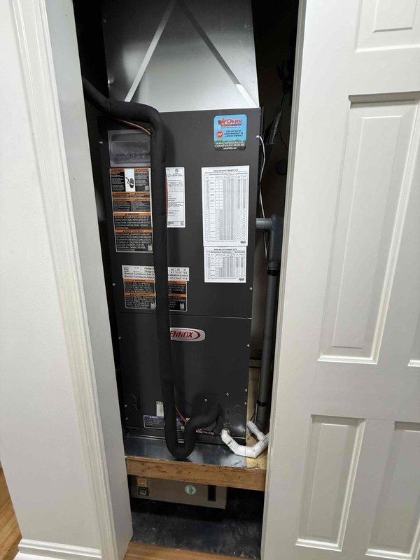 Completed installation of a 3-ton, 19 SEER Lennox heat pump system including outdoor condensing unit and indoor air handler. The air handler was installed vertically in an interior mechanical closet with proper PVC condensate drainage, supply/return ductwork connections, and all manufacturer safety labels intact. The outdoor heat pump unit was positioned in the residential yard with adequate clearance for airflow and service access, with all technical specifications, refrigerant warnings, and coil maintenance notices properly displayed per manufacturer requirements.