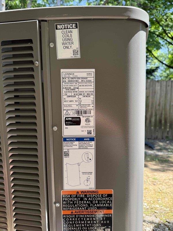 Completed installation of a 3-ton, 19 SEER Lennox heat pump system including outdoor condensing unit and indoor air handler. The air handler was installed vertically in an interior mechanical closet with proper PVC condensate drainage, supply/return ductwork connections, and all manufacturer safety labels intact. The outdoor heat pump unit was positioned in the residential yard with adequate clearance for airflow and service access, with all technical specifications, refrigerant warnings, and coil maintenance notices properly displayed per manufacturer requirements.