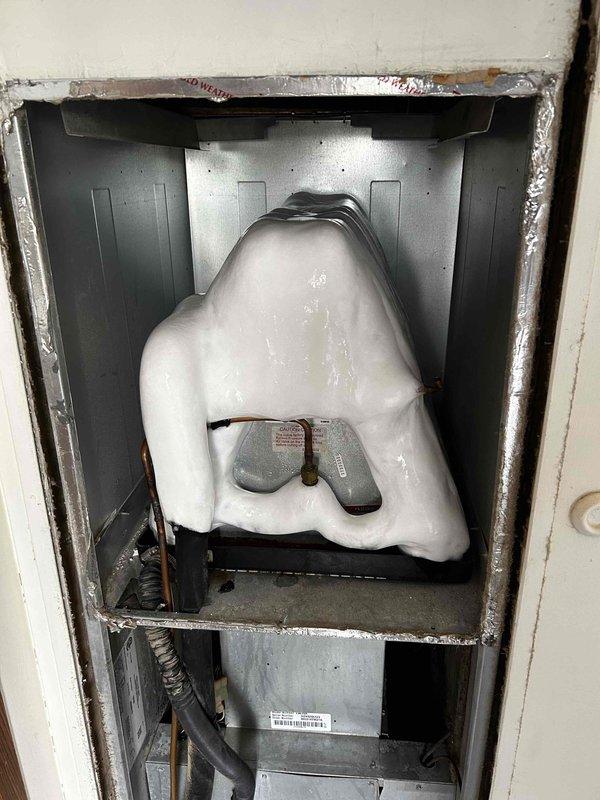Responded to no cooling complaint on 5-year-old residential HVAC system with indoor temperature at 79°F. Upon inspection, discovered extensive ice buildup on evaporator coil, indicating restricted airflow or low refrigerant charge. Documented ice-covered coil assembly with substantial frost accumulation obscuring coil fins and internal components. Instructed homeowner to turn AC off and set fan to ON position to allow coil to defrost before further diagnostic work could be performed. System requires follow-up service after defrost cycle to diagnose underlying cause of freezing condition, which may include dirty air filter, blocked return air, low refrigerant charge, or failed blower motor components.