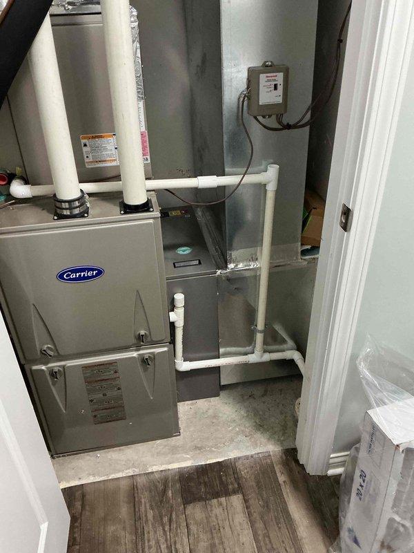 Completed follow-up site visit to inspect HVAC installation work in progress. Documented Carrier air handler unit properly positioned in mechanical closet with white PVC condensate drain lines installed vertically and horizontally from unit. Verified electrical control box mounted on wall with wiring connections in place. Photographed unfinished interior space showing exposed metal framing and ductwork requiring completion of remaining installation work.