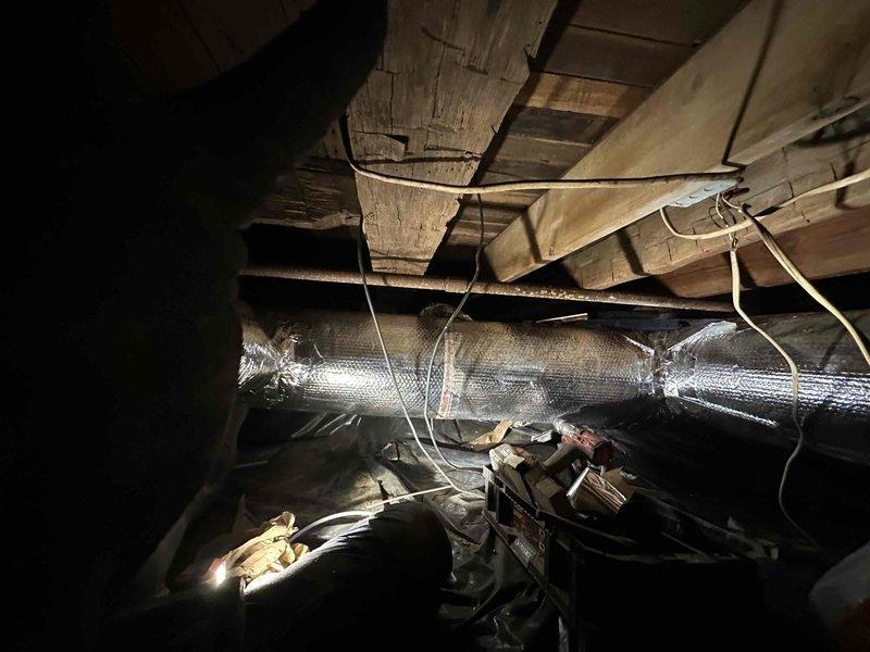 Completed full ductwork installation in crawl space area beneath residential structure. Installed insulated flexible ductwork throughout the underfloor space, properly secured with strapping to wooden floor joists to ensure stable positioning and prevent sagging. Routed ductwork to optimize airflow distribution while navigating existing electrical wiring and structural support elements. All ductwork wrapped with reflective silver insulation material to maximize energy efficiency and prevent condensation issues in the unconditioned crawl space environment. Installation completed in accordance with HVAC industry standards for residential duct systems.