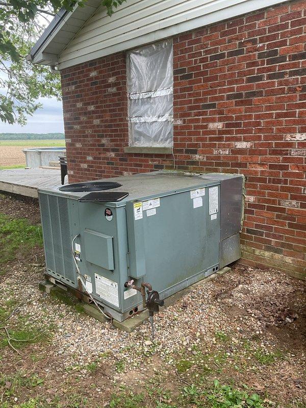 Completed comprehensive HVAC replacement estimate for residential property equipped with outdoor package unit showing significant weathering, surface corrosion, mineral deposits, and algae growth indicating extended service life and moisture exposure. Documented existing system condition including deteriorated cabinet surfaces, water staining, and biological growth at wall interface points. Provided detailed assessment and replacement recommendations for aging equipment positioned on ground-level gravel pad adjacent to brick foundation.