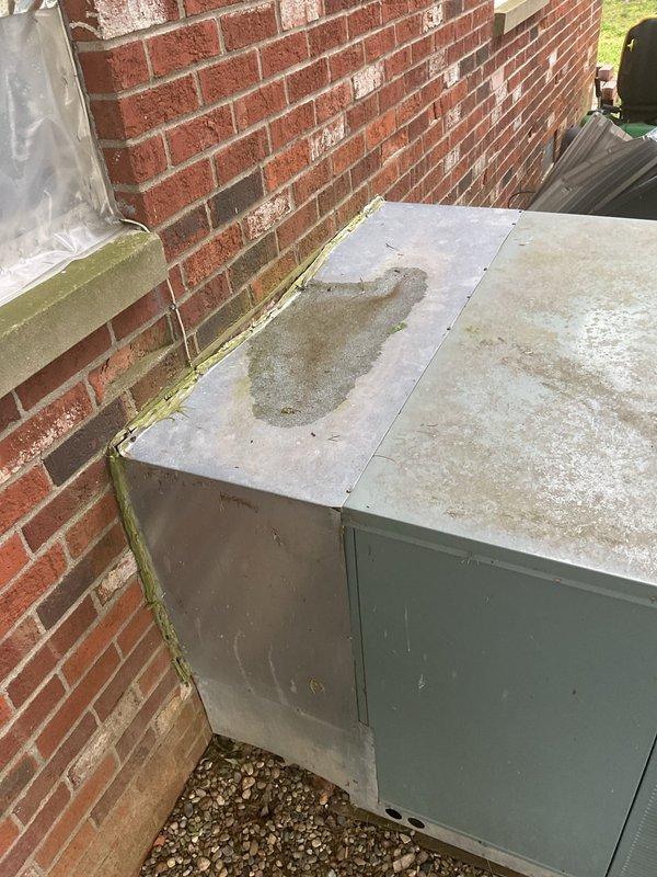 Completed comprehensive HVAC replacement estimate for residential property equipped with outdoor package unit showing significant weathering, surface corrosion, mineral deposits, and algae growth indicating extended service life and moisture exposure. Documented existing system condition including deteriorated cabinet surfaces, water staining, and biological growth at wall interface points. Provided detailed assessment and replacement recommendations for aging equipment positioned on ground-level gravel pad adjacent to brick foundation.