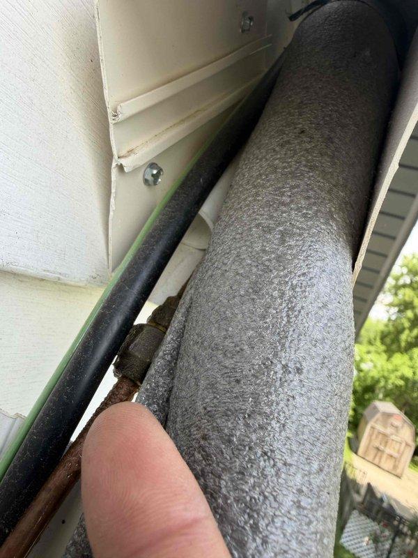 Responded to water leak concern on exterior of residence where condensate drain line was reported to be overflowing and dripping onto window sill. Upon inspection, located condensate drainage piping on side of building beneath eave. Examined refrigerant line set and condensate drain routing from HVAC system. Found deteriorated insulation on copper refrigerant lines with black foam insulation split and separated from piping, exposing underlying insulation material. Assessed condensate drain line installation and verified proper pitch and drainage flow. Inspected mounting brackets and pipe penetrations through building exterior. Confirmed condensate removal system was functioning correctly with no active overflow condition present at time of service. Documented existing condition of exterior piping insulation showing weather deterioration and recommended monitoring for future maintenance needs.