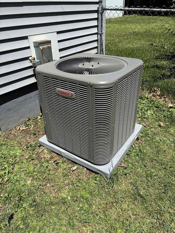 Completed installation of a 2.5-ton, 15.5 SEER Lennox air conditioning system including outdoor condenser unit and indoor air handler. The outdoor unit was positioned on a concrete pad against the building exterior with proper clearances, and the indoor air handler was installed in the basement utility area with copper refrigerant lines connecting both components.