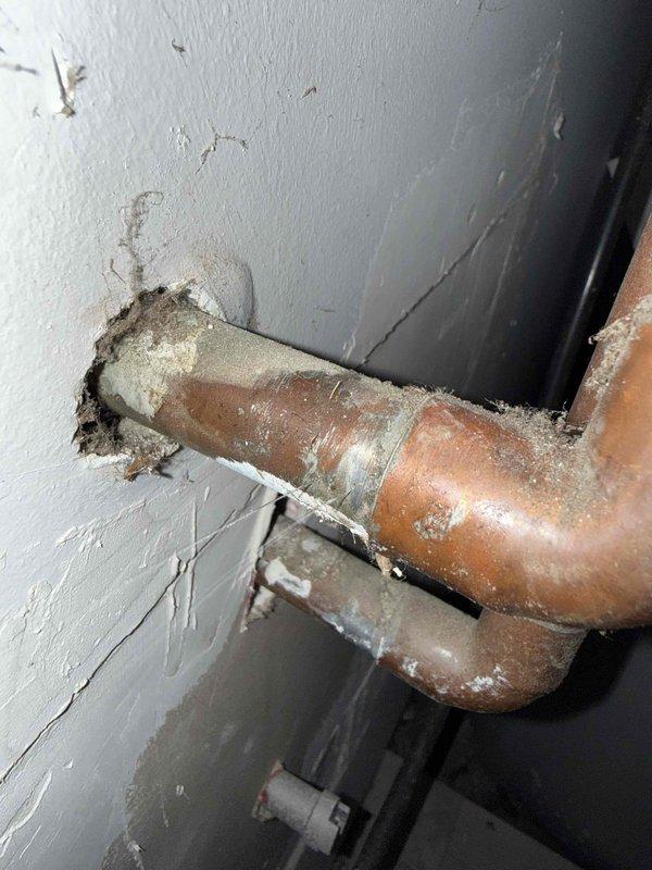 Responded to water leak call at residential property with 3-year-old HVAC system. Upon arrival, located active leak in garage area with significant water accumulation on floor. Inspected copper piping penetrating through wall and identified severe corrosion and oxidation on copper lines with characteristic greenish-white patina and mineral deposits indicating advanced deterioration. Observed water damage to surrounding wall surfaces with crumbling drywall material around pipe penetration points. Documented corroded copper piping conditions showing compromised integrity due to age and environmental exposure. Assessed leak source and extent of water intrusion affecting garage area.
