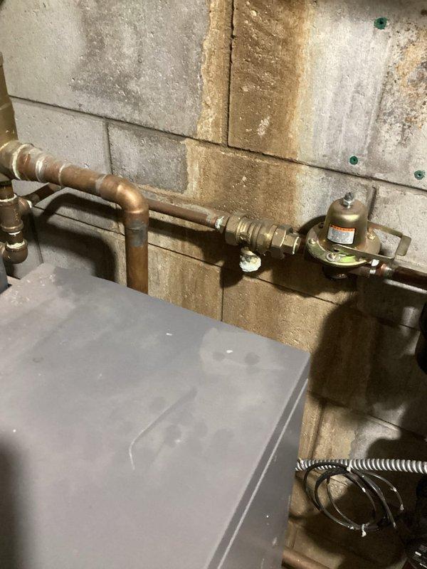Provided comprehensive plumbing estimate for kitchen reconfiguration and boiler system maintenance in residential basement utility area. Scope included relocating refrigerator water supply lines, installing new gas line routing for stove repositioning, and replacing critical boiler components including water filter, bell housing, and backflow prevention device. Existing copper piping infrastructure showed significant age-related patina and weathering, with basement walls displaying moisture staining patterns indicating previous water exposure. Current installation features aged pressure regulator, oxidized copper supply lines, and standard residential water heater configuration with overhead structural support systems requiring navigation during installation work.