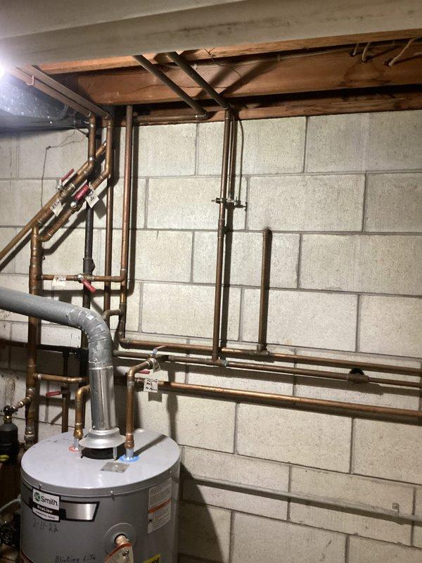 Provided comprehensive plumbing estimate for kitchen reconfiguration and boiler system maintenance in residential basement utility area. Scope included relocating refrigerator water supply lines, installing new gas line routing for stove repositioning, and replacing critical boiler components including water filter, bell housing, and backflow prevention device. Existing copper piping infrastructure showed significant age-related patina and weathering, with basement walls displaying moisture staining patterns indicating previous water exposure. Current installation features aged pressure regulator, oxidized copper supply lines, and standard residential water heater configuration with overhead structural support systems requiring navigation during installation work.