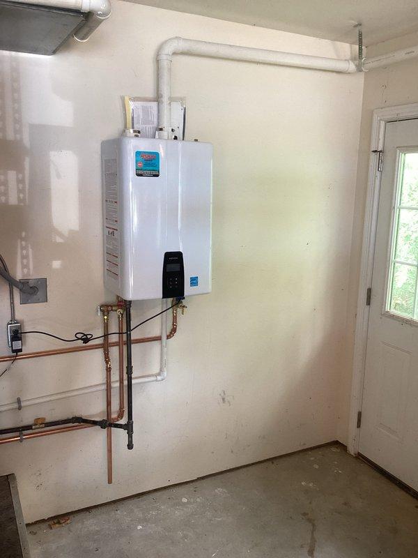 Completed installation of Energy Star-rated tankless water heater in interior utility room. Mounted unit to wall with proper structural support, connected copper supply and return lines with brass shutoff valves and fittings, and installed white PVC venting system routed through ceiling for proper exhaust ventilation. Wired electrical connections and control components to ensure safe operation. All plumbing connections tested and verified leak-free with proper water pressure and flow rates.