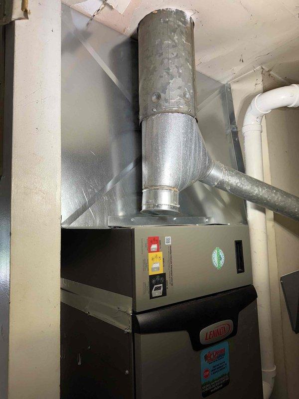 Completed installation of 2.5-ton, 15.5 SEER air conditioning system with 97% AFUE gas furnace in residential basement utility area. The new Lennox heating and cooling system was installed alongside existing water heater, with proper ductwork connections, condensate drainage routing via white PVC piping, and all required safety labeling in place. System was installed to manufacturer specifications with metallic supply duct trunk line extending from furnace cabinet to distribution points throughout the home.