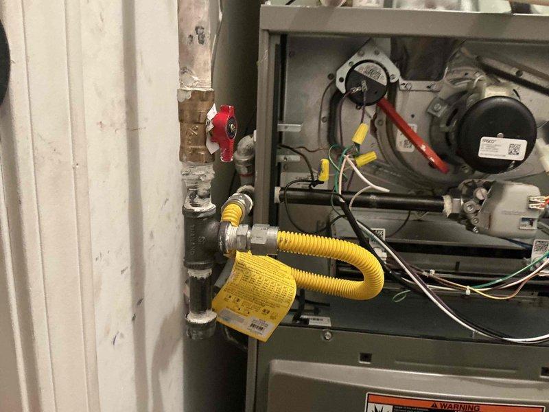 Responded to emergency gas leak call for dual-system residential HVAC installation. Upon arrival, confirmed strong constant gas odor inside structure near furnace location. Gas utility company had previously shut off meter valve due to leak detection. Performed comprehensive leak detection inspection of gas supply lines, connections, and furnace manifold using electronic leak detector and soap bubble solution. Identified leak at yellow flexible gas connector (CSST) connection point at furnace inlet. Inspected black iron pipe gas supply line, red shutoff valve, and all threaded fittings for additional leak sources. Verified proper torque and thread sealant application on all gas line connections. Tightened loose flex connector fitting and re-tested connection points. Conducted complete system pressure test to verify leak repair integrity. Inspected furnace internal components including blower motor, electrical connections, and burner assembly for proper operation and safety compliance. 