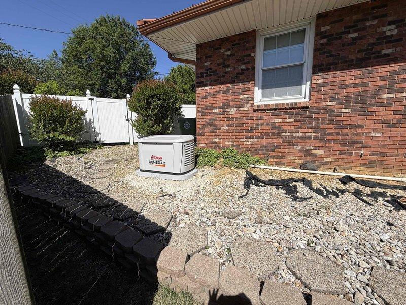 Completed installation of an 18kW Generac standby generator system at residential property. Unit was positioned on prepared gravel pad adjacent to house foundation with proper clearances maintained from structure and property boundaries. Leveling procedures were performed using precision instruments to ensure generator sits on stable, level concrete base per manufacturer specifications. All electrical connections were made in accordance with NEC requirements, including proper bonding and grounding of the system. Generator placement allows adequate ventilation clearance and accessibility for future maintenance while maintaining aesthetic integration with existing landscaping and privacy fencing.