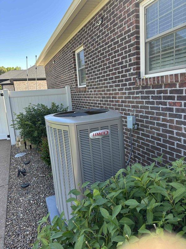 Completed full HVAC system installation featuring a 4-ton, 18 SEER Lennox air conditioning unit with 99% efficiency heating system. The outdoor condenser was professionally mounted on a concrete pad with gravel base against the brick foundation, with refrigerant lines and electrical conduits neatly routed vertically along the exterior wall to the roofline. All components were installed to manufacturer specifications, system was charged, tested, and verified operational.