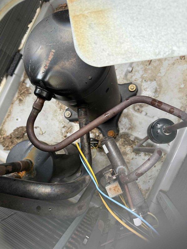 Responded to no cooling complaint on 12-year-old Carrier system where blower was operational but unit failed to produce cool air. Upon inspection, discovered outdoor condenser unit not running due to failed compressor and associated electrical issues, evidenced by significant corrosion on refrigerant lines, accumulator, and condenser components. System showed signs of age-related deterioration including rust staining on cabinet panels and oxidation on copper refrigerant piping connections. Performed diagnostic testing to confirm compressor failure and assessed overall system condition, noting indoor air handler unit in utility room remained functional with adequate airflow through vents.