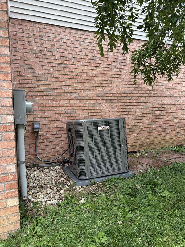 # HVAC Complete System Installation

Successfully completed installation of a 3.5-ton, 15.5 SEER air conditioning system paired with a 97% AFUE gas furnace at residential property. Installed Lennox outdoor condensing unit on concrete pad with proper leveling and clearances. Unit positioned on exterior brick wall with decorative rock landscaping base. Mounted weatherproof electrical disconnect box on exterior wall with appropriate conduit and wiring per code requirements. Routed refrigerant line set through brick wall penetration with proper sealing.

Interior installation completed in utility room with equipment mounted on elevated brick platform for drainage and accessibility. Installed complete air handler system with vertical configuration to maximize space efficiency. Integrated new furnace unit with existing ductwork connections. Mounted humidification system components including metallic cylindrical humidifier assembly near ceiling level. All equipment secured with proper mountin