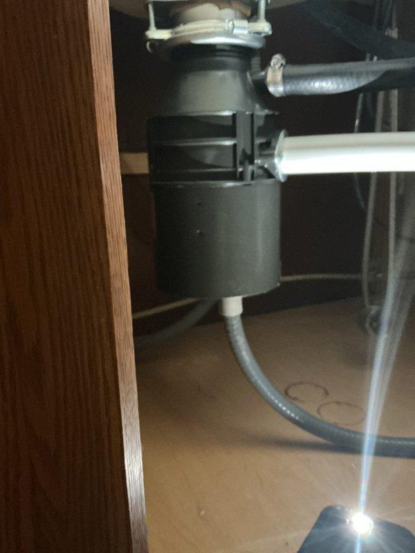 Performed comprehensive plumbing inspection at a 21-year-old residential property to diagnose a non-functioning garbage disposal and leaking kitchen faucet. Conducted visual assessment of the InSinkErator-style disposal unit mounted beneath the kitchen sink, examining electrical connections, reset button, mounting assembly, and discharge plumbing. Inspected the flexible corrugated drain line connection and verified proper alignment with the waste line system. Evaluated the brushed nickel kitchen faucet for leak source, checking supply line connections, cartridge integrity, O-rings, and aerator assembly. Documented existing plumbing configuration including white PVC drain system and under-sink cabinet conditions through photographic evidence. Provided detailed findings and repair recommendations to address both the inoperative disposal unit and the persistent faucet leak that had been occurring for approximately two weeks.