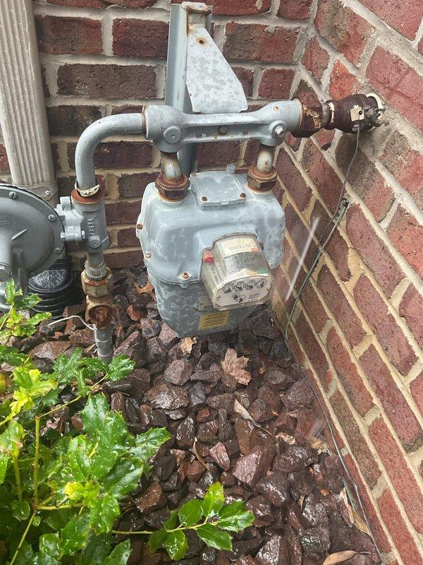 Conducted comprehensive electrical estimate for standby generator installation at residential property. Performed site assessment and documented existing natural gas infrastructure, including meter location, pipe configuration, and connection points on exterior brick wall. Evaluated gas supply system condition, noting existing meter assembly with multiple pipe connections, shut-off valves, and brass fittings showing age-related corrosion at joints and connection points. Assessed available fuel source for generator operation and confirmed natural gas availability through existing utility meter. Documented meter placement relative to structure for determining optimal generator positioning and fuel line routing. Evaluated electrical service panel accessibility and capacity for generator integration. Photographed existing gas infrastructure to support equipment sizing calculations and installation planning. Reviewed site conditions including clearance requirements, ventilation consideratio