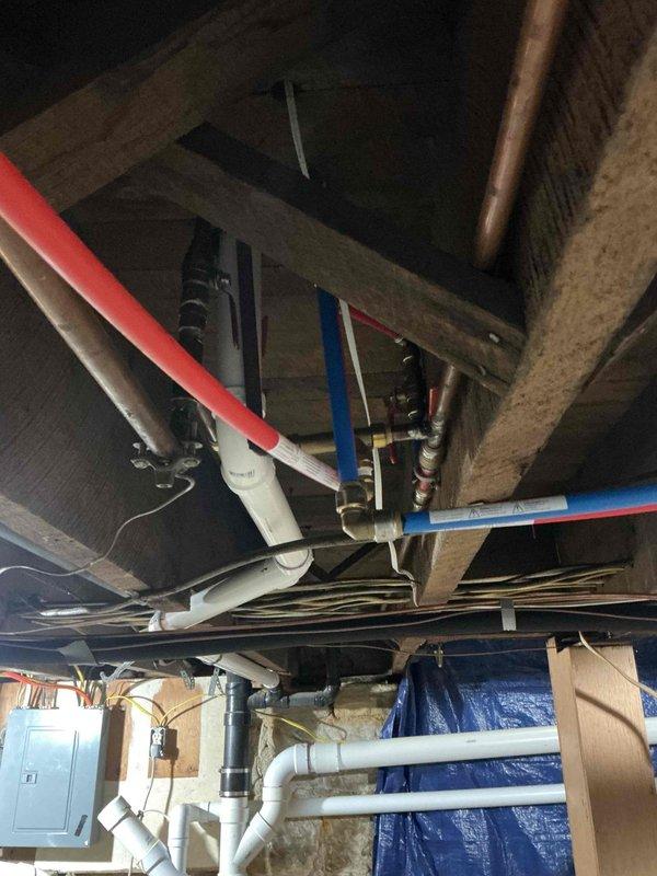 Conducted follow-up assessment for water heater replacement options in basement location. Evaluated existing mechanical infrastructure including current water heater installation located under stairs, plumbing supply and drainage lines, gas connections, and available space for upgraded equipment. Documented basement ceiling area showing existing PVC water supply lines with insulation, drainage piping, ductwork, and structural joists to determine routing requirements for new installation. Assessed utility room configuration with concrete block walls and existing mechanical equipment to verify clearances and ventilation requirements. Prepared comprehensive estimates for two replacement scenarios: traditional tank-style gas water heater and tankless gas water heater system, both sized appropriately for increased capacity needs. Recommendations include removal of current under-stairs unit and installation of larger capacity system in basement location with proper venting, gas line modifica