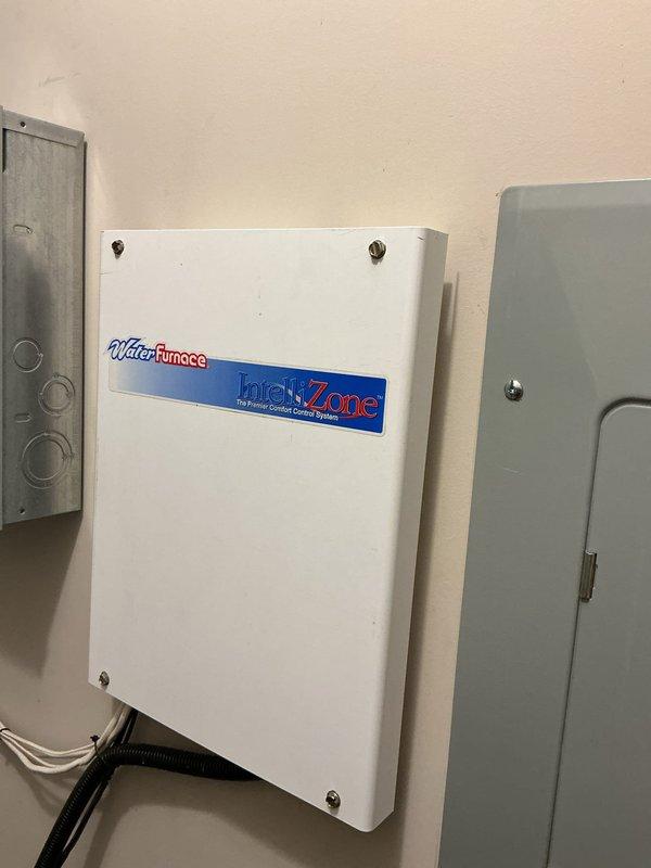 Responded to no cooling complaint on 23-year-old WaterFurnace geothermal system with IntelliZone zoned comfort control. System was providing insufficient cooling to entire home. Performed diagnostic evaluation of geothermal heat pump, air handler, and zone control system. Inspected compressor operation, refrigerant circuit, water loop connections, and airflow distribution through black flex duct connections. Verified no ice buildup on coils and confirmed system was operational but not meeting capacity demands. Documented existing equipment configuration including gray insulated air handler and white zone control junction connections. Discussed system age, declining performance characteristics typical of equipment exceeding 20-year service life, and provided customer with replacement options including Bosch, Geo Comfort, and ClimateMaster geothermal systems as alternatives to continued repairs on aging equipment.