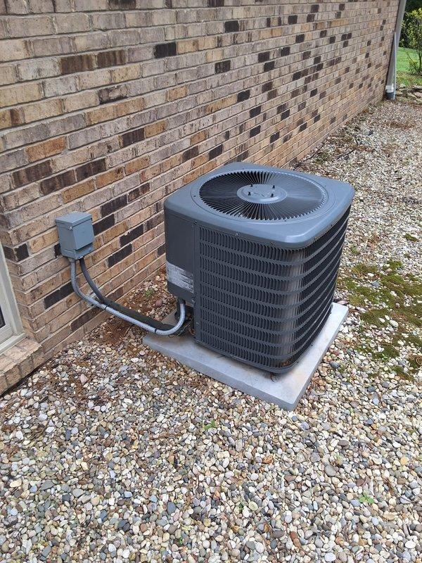 # HVAC Service Call: Air Conditioning System Inspection

Responded to service call for residential air conditioning unit experiencing ice formation on refrigerant line while system continued to operate. Upon arrival, confirmed customer had properly shut down compressor and left fan running as previously instructed.

Performed comprehensive inspection of 12-year-old AC system. Examined outdoor condensing unit positioned on concrete pad against exterior wall, noting unit construction with horizontal fin louvers and top-mounted fan assembly. Verified electrical disconnect box and conduit connections at wall mount. Documented equipment specifications and manufacturer information visible on unit nameplate.

Conducted interior electrical panel inspection, photographing circuit breaker configuration and panel directory for service records. Assessed dual-row breaker arrangement and verified proper labeling documentation.

Ice formation on suction line typically indicates restricted airflow, lo