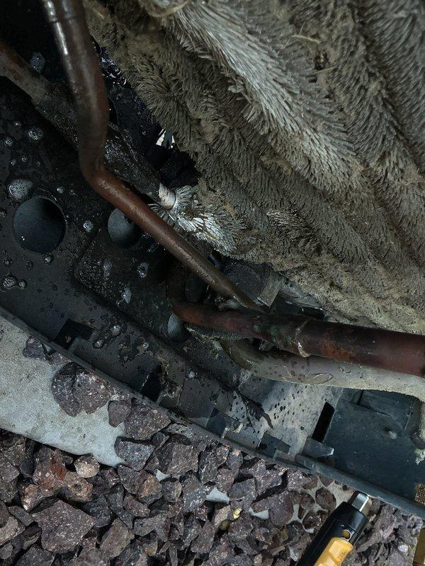 Responded to callback for HVAC system failure following previous service visit where condensate drain line was found disconnected from clamp and improperly pitched, causing water infiltration into blower motor assembly. Upon arrival, unit was non-operational. Inspection revealed significant corrosion and leak in condenser coil, confirmed through visual examination. Photographed affected areas showing deteriorated copper piping with oxidation, extensive dust and debris accumulation on evaporator coil fins, moisture presence throughout system, and sediment deposits on unit base. System requires condenser coil replacement to restore proper operation and prevent continued refrigerant loss.