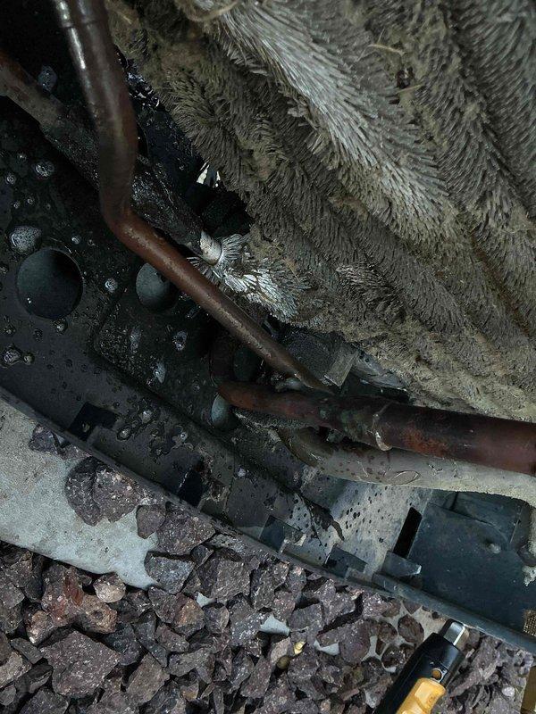 Responded to callback for HVAC system failure following previous service visit where condensate drain line was found disconnected from clamp and improperly pitched, causing water infiltration into blower motor assembly. Upon arrival, unit was non-operational. Inspection revealed significant corrosion and leak in condenser coil, confirmed through visual examination. Photographed affected areas showing deteriorated copper piping with oxidation, extensive dust and debris accumulation on evaporator coil fins, moisture presence throughout system, and sediment deposits on unit base. System requires condenser coil replacement to restore proper operation and prevent continued refrigerant loss.