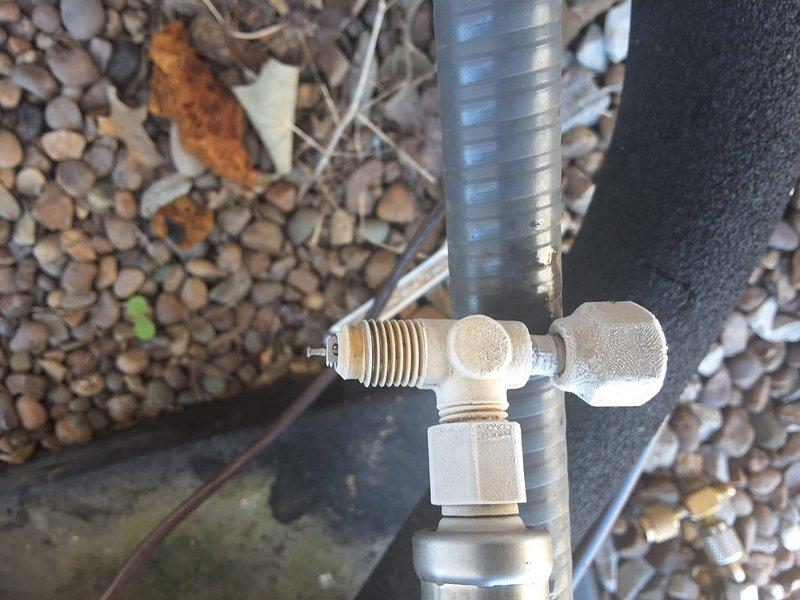Responded to service callback for inadequate cooling with system running but unable to maintain setpoint. Unit was operating with thermostat set to 68°F but space temperature reading 74°F. Inspected outdoor unit connections and refrigerant line set. Examined brass service valves, flexible line connections, and insulated piping at outdoor equipment. Documented condition of refrigerant fittings showing mineral deposits and weathering consistent with outdoor exposure. Verified all mechanical connections at valve assemblies and junction points. System components photographed for service records showing T-fitting connections, corrugated line set, and foam pipe insulation at exterior installation location.