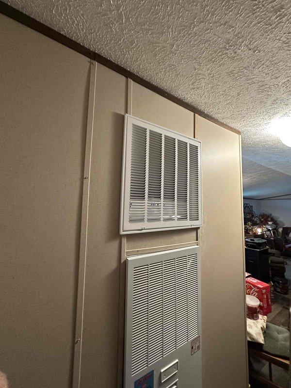 Completed follow-up site visit to document previously installed through-the-wall HVAC system. Verified proper installation of wall-mounted air handler unit with return air grille positioned above the unit, confirmed digital thermostat control panel is operational with illuminated display, and captured photographic documentation of the completed installation showing flush-mounted unit integration with surrounding wall structure.