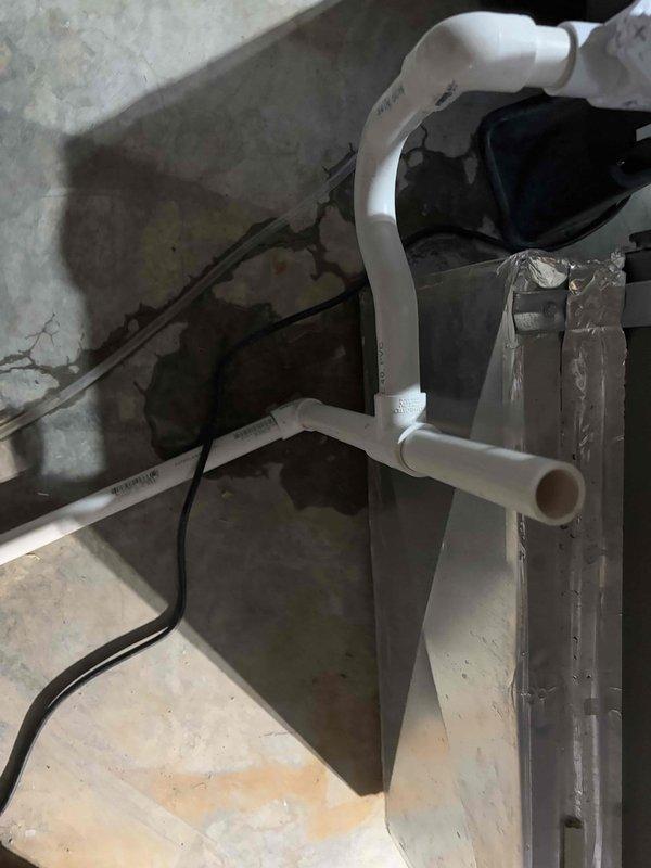 Responded to callback for recurring system leak following previous service visit. Upon arrival, inspected condensate drain system and discovered compromised drain line connections causing water accumulation on concrete floor. Evaluated condensate pump operation and drain pan assembly at air handler base. Identified improper trap configuration and potential blockage in PVC drain lines contributing to overflow condition. Documented water staining patterns on floor indicating ongoing drainage issue. Photographed condensate management system including pump, drain pan, and PVC piping assembly for further assessment and recommended corrective action to resolve persistent leakage problem.