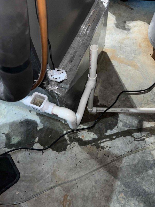 Responded to callback for recurring system leak following previous service visit. Upon arrival, inspected condensate drain system and discovered compromised drain line connections causing water accumulation on concrete floor. Evaluated condensate pump operation and drain pan assembly at air handler base. Identified improper trap configuration and potential blockage in PVC drain lines contributing to overflow condition. Documented water staining patterns on floor indicating ongoing drainage issue. Photographed condensate management system including pump, drain pan, and PVC piping assembly for further assessment and recommended corrective action to resolve persistent leakage problem.