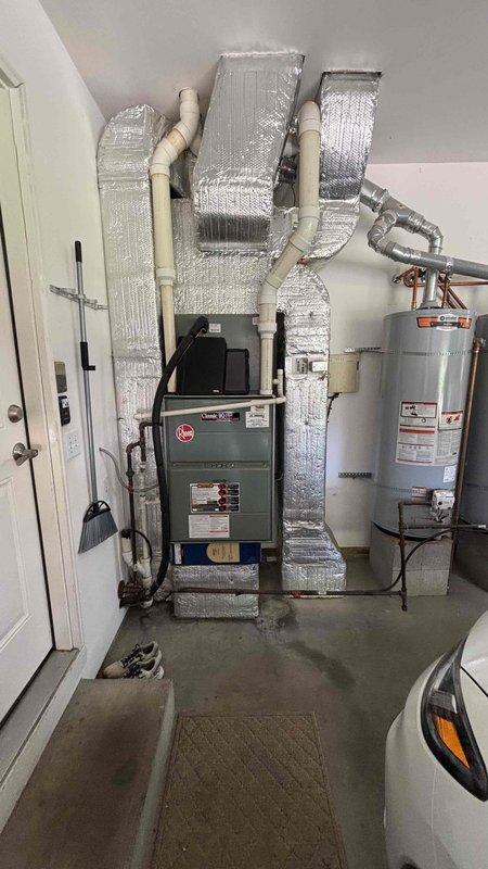 Conducted comprehensive HVAC replacement estimate at residential property with existing furnace, air handler, and dual water heater installation located in garage utility area. Evaluated current system performance issues as homeowner reported equipment not operating efficiently. Assessed existing gray furnace unit with reflective foil insulation wrapping, vertical-mounted air handler with silver ductwork, and dual cylindrical water heaters for replacement specifications. Documented equipment configuration, ductwork routing, utility connections, and installation space constraints. Photographed current system layout including furnace positioning, air handler mounting, water heater placement, PVC piping, electrical panel access, and available clearances for new equipment installation. Reviewed replacement options with homeowner present during appointment. Provided detailed specifications and recommendations for complete HVAC system replacement to address performance concerns and improve o