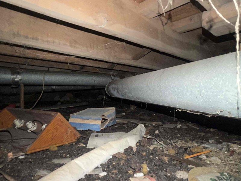 Responded to water leak in basement utility area affecting 1-year-old HVAC system with steady drip migrating toward foundation. Inspected crawlspace and identified compromised drainage system requiring replacement. Documented water damage on wooden flooring near vertical PVC drainage pipes and mechanical equipment. Scheduled follow-up service to rerun drain line using approximately 20 feet of 3/4" PVC pipe and install 20 feet of heat tape for freeze protection. Photographed crawlspace conditions showing debris accumulation and existing drainage configuration, as well as utility closet area displaying water staining on floor surfaces adjacent to plumbing connections.