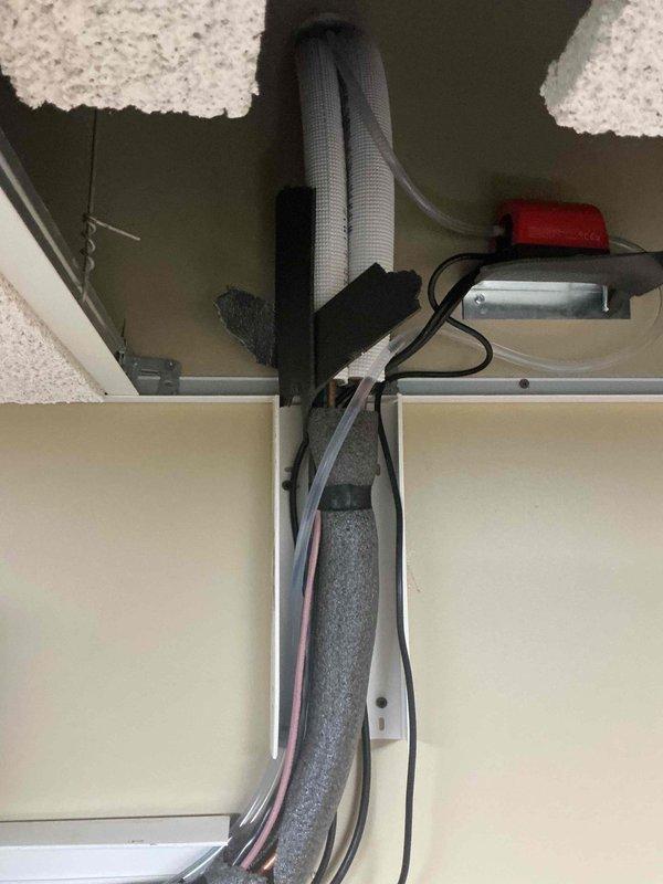 Completed follow-up site visit to investigate and document reported water leak condition. Inspected HVAC system installation including refrigerant line insulation, condensate drainage routing, and air handler unit operation. Documented existing pipe insulation configuration with gray foam covering refrigerant lines secured with mounting straps in ceiling cavity. Verified air handler unit displaying 70° on digital readout and confirmed proper flexible duct connection to ceiling plenum. Photographed electrical wiring routing, safety switch mounting, and overall system component placement for service records. No active water leak observed at time of inspection; all insulated lines and connections appeared dry with no visible moisture damage to surrounding ceiling materials or equipment surfaces.