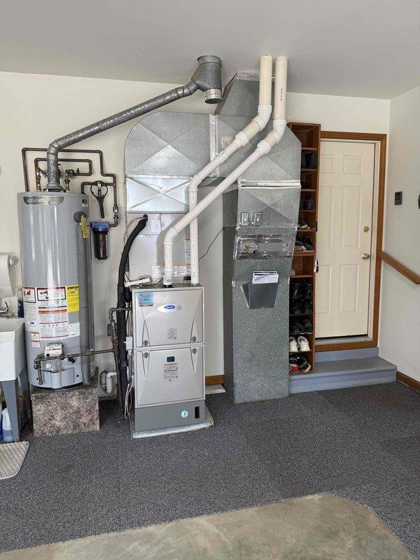 Completed full HVAC system changeout, removing existing Lennox equipment and installing new Carrier system per specifications. Installed Carrier furnace in interior utility room with proper venting and condensate drainage using white PVC piping. Mounted new air handler with integrated ductwork, connecting gray flexible duct for proper airflow distribution. Positioned equipment to maintain clearances and accessibility for future service. 

Installed Carrier outdoor condensing unit on exterior brick wall, setting unit on composite pad over gravel base for proper drainage and vibration isolation. Connected electrical service with exterior disconnect box and appropriate conduit routing. Verified all refrigerant line connections, electrical wiring, and control circuits for proper operation. System startup completed with all components functioning within manufacturer specifications.
