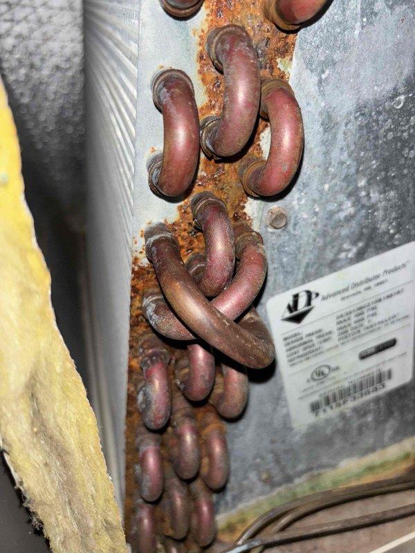 # HVAC Service Completion Summary

Responded to service call for 9-year-old AC system with reported cooling failure and condenser leak. Upon inspection, discovered severely corroded copper refrigerant tubing at evaporator coil connections with active leak points. Extensive rust and corrosion present on tubing bends and mounting plate, indicating prolonged moisture exposure. Documented condition of outdoor condensing unit and compromised indoor coil assembly. System requires refrigerant line replacement and evaporator coil evaluation due to extent of corrosion damage affecting system integrity and cooling performance.