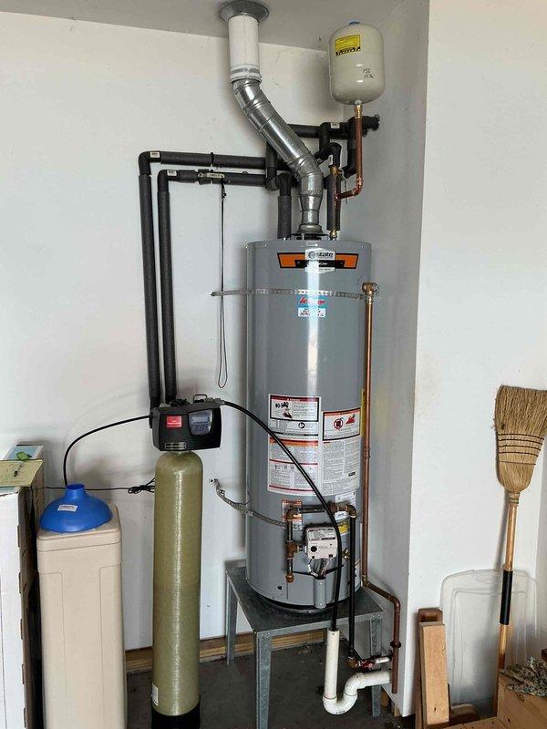 Installed a 40-gallon gas tall water heater (57 1/2" height x 21" width) in residential utility area. Unit was mounted on metal stand with proper venting system including flexible metallic ductwork and stainless steel exhaust assembly extending through ceiling penetration. Connected copper supply lines with brass compression fittings to existing plumbing infrastructure, installed white expansion tank with proper pressure relief configuration, and integrated system with existing water softener unit. All connections were secured and tested for proper operation. Installation includes 6-year parts and 1-year labor warranty.