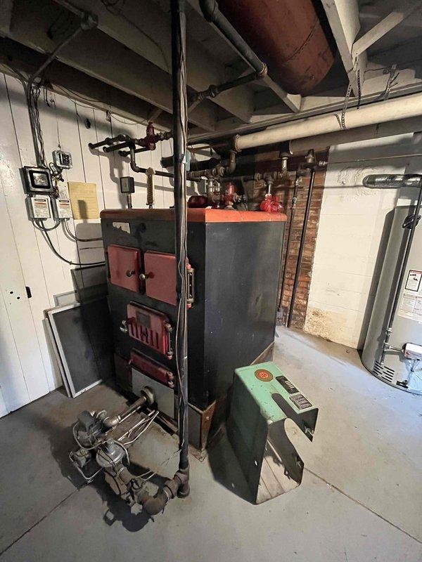 Conducted comprehensive on-site assessment of existing residential boiler system for replacement estimate. Evaluated aged boiler unit with associated piping, control valves, circulator pump, and electrical components. Documented current system configuration including red-handled control valve assembly with threaded brass connections, vintage boiler with multiple supply and return lines, basement mechanical room layout, and existing ductwork infrastructure. Photographed equipment conditions showing signs of age and wear on control mechanisms and boiler surfaces. Assessed mechanical room accessibility, structural considerations, and existing utility connections to provide accurate replacement specifications and recommendations.