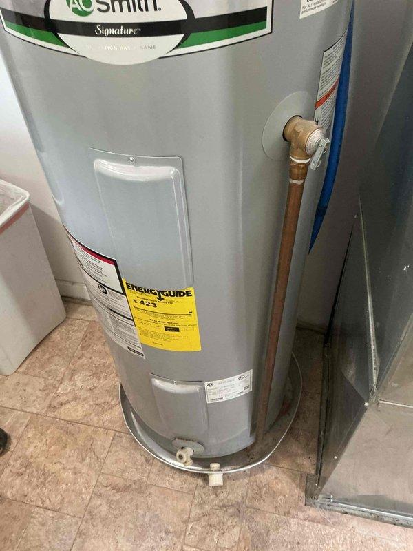 Completed on-site estimate for 40-gallon gas water heater replacement. Assessed existing A.O. Smith Signature gas water heater located in utility area with tile flooring, noting current copper piping connections and brass fittings. Documented exterior venting system including light blue PVC pipe extending through landscaped area near building foundation. Photographed unit specifications, energy rating labels, and current installation configuration to provide comprehensive replacement estimate. Confirmed gas fuel type and verified accessibility for future installation work.
