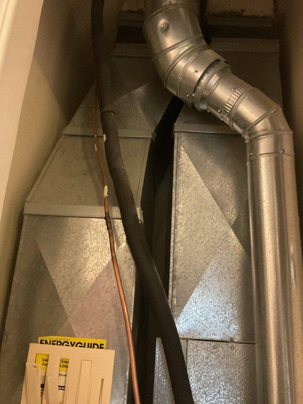 Completed comprehensive HVAC system evaluation for replacement estimate on fifteen-year-old air conditioning system. Documented existing equipment configuration including air handler unit with galvanized metal ductwork, copper refrigerant lines, and thermostat wiring setup. Photographed current installation showing metal supply plenum with curved elbow transition, existing control wiring with multiple zone connections at thermostat terminals, and overall system layout in basement utility area to provide accurate replacement specifications and equipment recommendations.