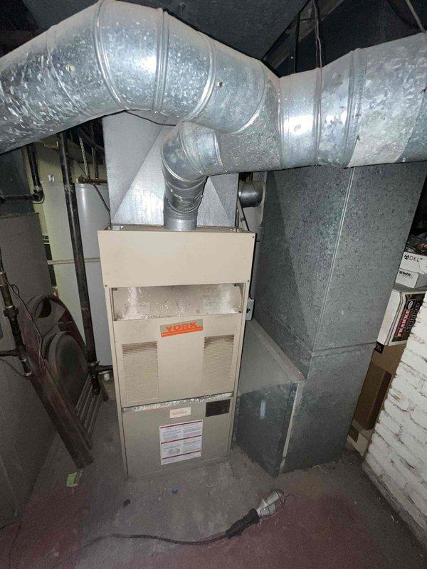 Conducted comprehensive assessment of existing HVAC system in residential duplex property for full replacement estimate. Both heating and air conditioning units identified as original equipment dating from mid-1980s to early 1990s, approximately 33 years old. Inspected York furnace installation in basement mechanical room, evaluated condition of existing flexible ductwork with metallic insulation, and documented current system configuration including air handler, plenum connections, and refrigerant line routing. Photographed equipment nameplate information, ductwork layout, and overall installation setup to provide accurate replacement specifications and equipment sizing recommendations for aged heating and cooling system.