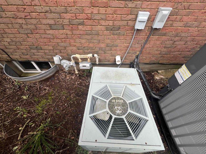 Conducted comprehensive site evaluation for residential cooling system replacement. Existing air conditioning unit assessed at 28 years of service life, having reached end of expected operational lifespan. Documented current outdoor condensing unit configuration, utility connections including gas meter proximity, electrical service boxes, refrigerant line routing, and condensate drainage system. Photographed equipment placement against brick structure with surrounding landscaping considerations for future installation planning. Provided detailed replacement estimate for new cooling system with recommendations for modern high-efficiency equipment upgrade.