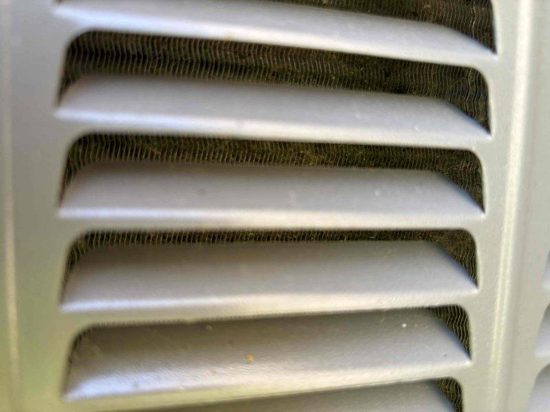 Completed annual planned maintenance on 6-month-old HVAC system during first scheduled visit. Inspected outdoor condenser unit and noted significant vegetation encroachment with plant stems and leaves obstructing airflow around louvers and top panel. Examined indoor evaporator coil assembly through ventilation grille, confirming proper fin condition and component integrity.