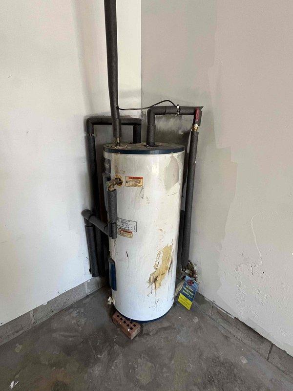 Completed on-site estimate for mini-split installation in garage and replacement of existing tank-style electric water heater with 40 or 50-gallon unit. Assessed current working water heater showing age-related wear and staining, documented existing plumbing connections and venting configuration, and evaluated garage space with exposed framing for ductless mini-split system placement.