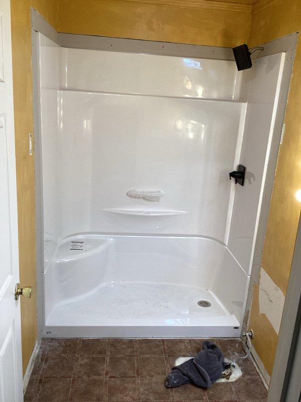 Two technicians completed a full-day installation of a new one-piece fiberglass shower enclosure in a bathroom corner. The scope included setting the molded shower base with integrated pan and drain assembly, securing the three-panel surround system with mounting hardware, reworking the drain connection to align with the new fixture, and installing drywall around the perimeter of the shower stall to enclose the unit. The drywall finishing, trim work, and shower fixture installation were left for subsequent completion.